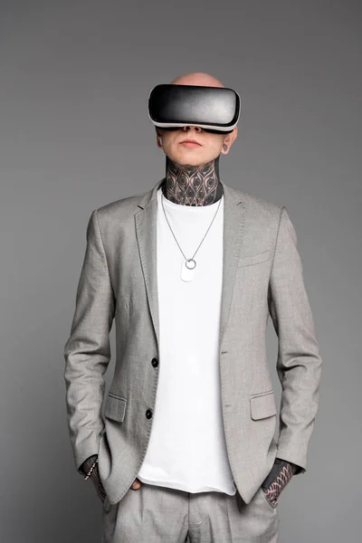 Stylische tätowierte Mann mit den Händen in den Taschen und mit Virtual-Reality-Headset isoliert auf grau — Stockfoto