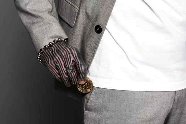 Cropped shot of tattooed man in suit putting bitcoin in pocket isolated on grey — Stock Photo