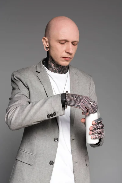 Лысый красивый татуированный мужчина в пиджаке, открывающий алюминиевую банку, изолированную на сером — стоковое фото