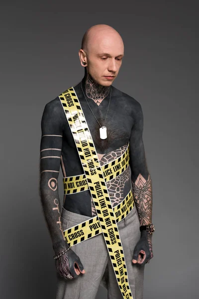 Homme à poitrine nue avec des tatouages et la ligne de police autour du corps regardant vers le bas isolé sur gris — Photo de stock