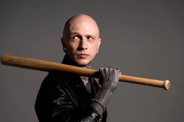 Tätowierter Mann mit Glatze in Lederjacke hält Baseballschläger in der Hand und schaut vereinzelt auf grau — Stockfoto