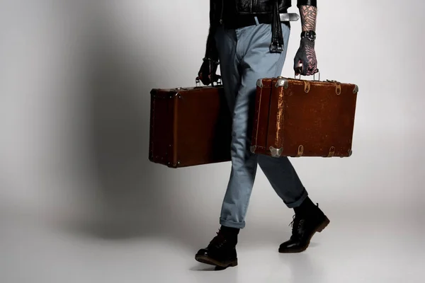 Low section of tattooed man in leather jacket walking with suitcases on grey — Stock Photo