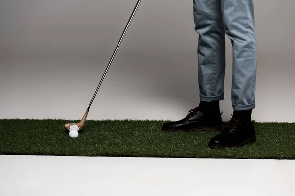 Sección baja del hombre en jeans y botas de cuero jugando al golf en césped artificial en gris - foto de stock