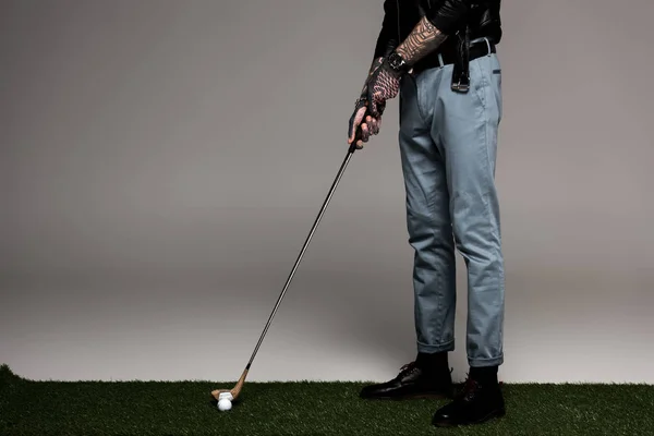 Низкая часть татуированного человека в джинсах и кожаной куртке играет в гольф на сером — стоковое фото