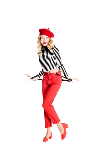 Smiling pretty woman in red beret and holding suspenders isolated on white — Stock Photo