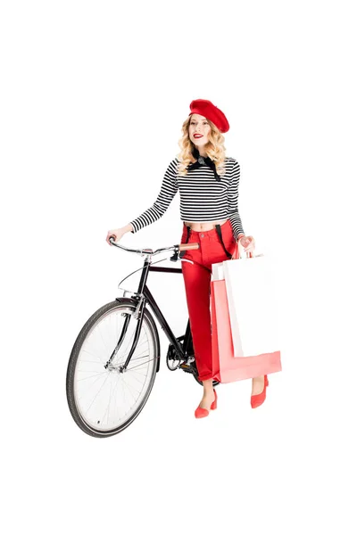 Mulher feliz segurando sacos de compras e sorrindo enquanto estava perto de bicicleta isolada no branco — Fotografia de Stock