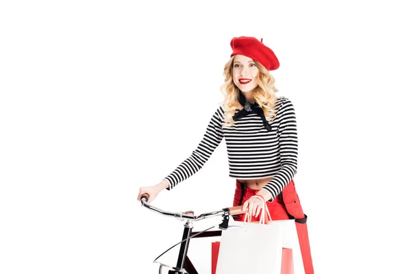 Jolie femme en béret rouge tenant des sacs à provisions près de vélo isolé sur blanc — Photo de stock