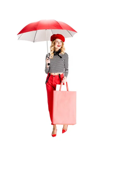 Hübsche Frau mit rotem Regenschirm, während sie mit Einkaufstaschen isoliert auf weiß steht — Stockfoto