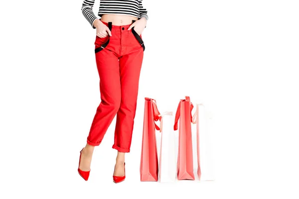 Cropped view of woman standing with hands in pockets near red shopping bags isolated on white — Stock Photo