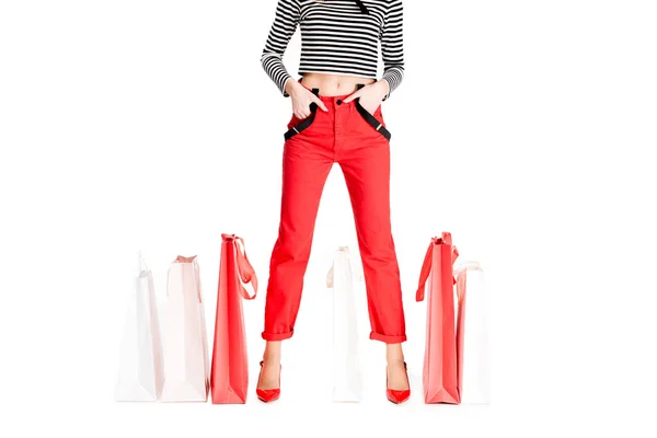 Vista cortada da mulher de pé com as mãos nos bolsos entre sacos de compras vermelhos isolados no branco — Fotografia de Stock