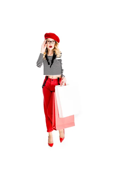 Surprised woman in glasses and red beret holding shopping bags isolated on white — Stock Photo