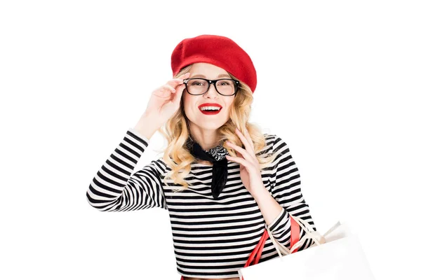 Sonriente mujer en boina roja y gafas sosteniendo bolsas aisladas en blanco - foto de stock