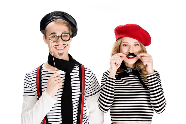 Smiling woman holding fake mustache near man with glasses on stick isolated on white — Stock Photo