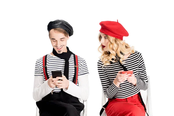 Française femme en béret regardant l'homme en utilisant smartphone tout en étant assis sur chaise isolé sur blanc — Photo de stock