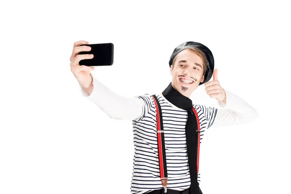 Alegre francés hombre en negro boina tomando selfie y mostrando pulgar hacia arriba signo aislado en blanco - foto de stock