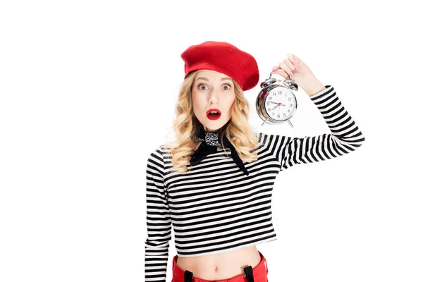 Mujer sorprendida en boina roja sosteniendo reloj despertador aislado en blanco - foto de stock