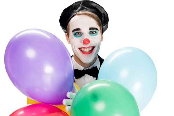 Веселый клоун в черном берете держит воздушные шары и улыбается изолированно на белом — стоковое фото