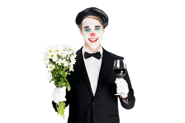 Payaso sonriente sosteniendo flores y vidrio en vino en manos aisladas en blanco - foto de stock