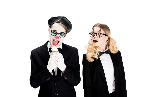 Joyeux clown en costume et lunettes regardant savoureux cupcake près de femme isolée sur blanc — Photo de stock