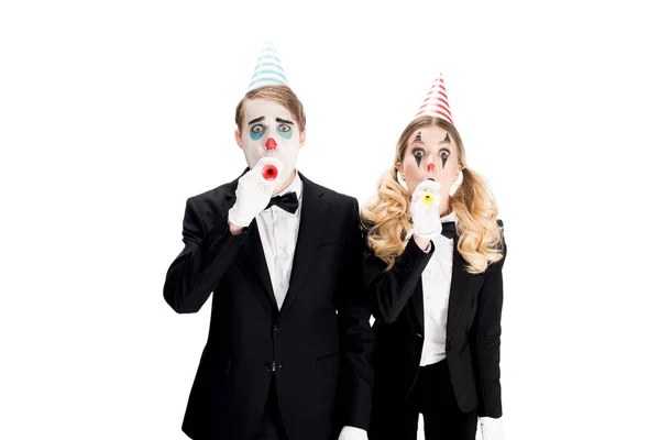 Пара клоунов в костюмах, дующих в праздничные вентиляторы, изолированные на белом — стоковое фото