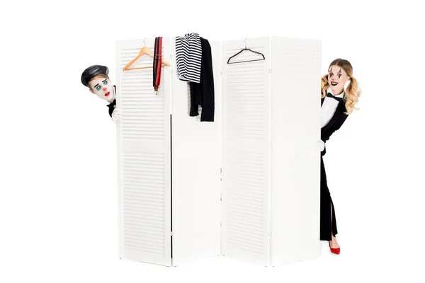 Femme souriante en costume regardant par la porte du vestiaire près du clown surpris isolé sur blanc — Photo de stock