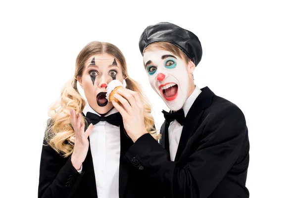 Pazzo clown lancio cupcake di fronte alla donna sorpresa isolato su bianco — Foto stock