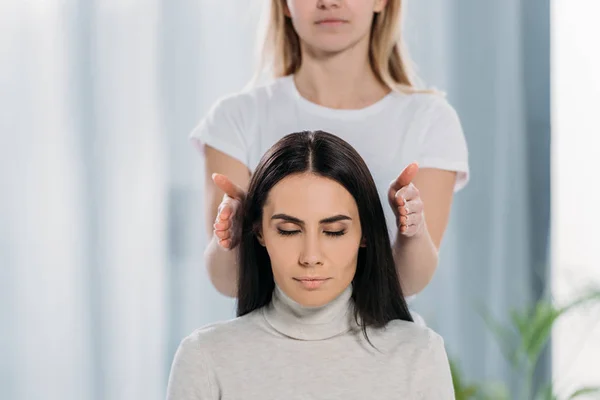 Abgeschnittene Aufnahme einer friedlichen jungen Frau mit geschlossenen Augen, die sitzt und eine Reiki-Heiltherapie erhält — Stockfoto