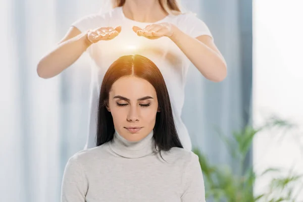 Peaceful young woman with closed eyes receiving reiki healing therapy above head — Stock Photo
