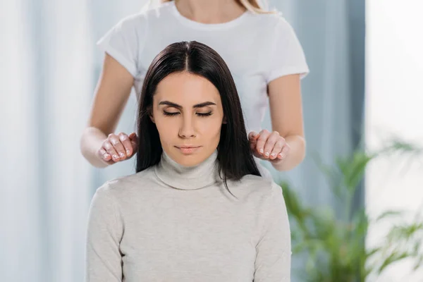 Tiro recortado de curandeiro do sexo feminino fazendo sessão de terapia reiki para a jovem mulher com olhos fechados — Fotografia de Stock