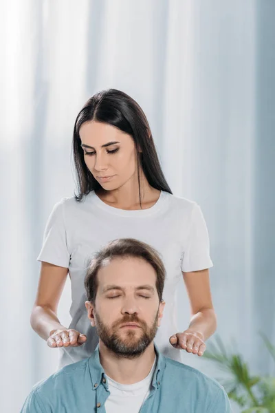 Молодая женщина делает Рейки сеанс терапии бородатый спокойный мужчина с закрытыми глазами — стоковое фото