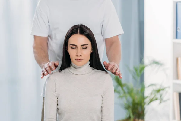 Cropped shot of calm young woman with closed eyes receiving reiki healing treatment on shoulders — Stock Photo