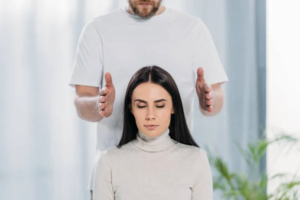 Tiro cortado de curandeiro barbudo fazendo sessão de terapia reiki para a jovem mulher com olhos fechados — Fotografia de Stock