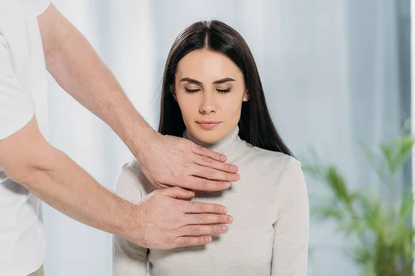 Tiro recortado de mulher jovem com os olhos fechados sentado e recebendo tratamento reiki no peito — Fotografia de Stock