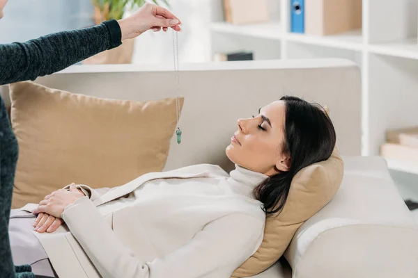 Обрізаний знімок гіпнотика з маятником гіпнотизуюча молода жінка лежить на дивані — стокове фото