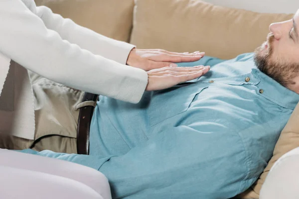 Cropped shot of bearded man lying on couch and receiving reiki treatment on chest — Stock Photo