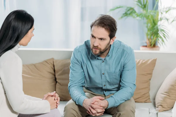 Giovane psicoterapeuta femminile e uomo barbuto sconvolto seduto e guardarsi l'un l'altro — Foto stock