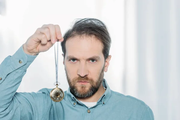 Serious bearded hypnotist holding dowsing and looking at camera — Stock Photo