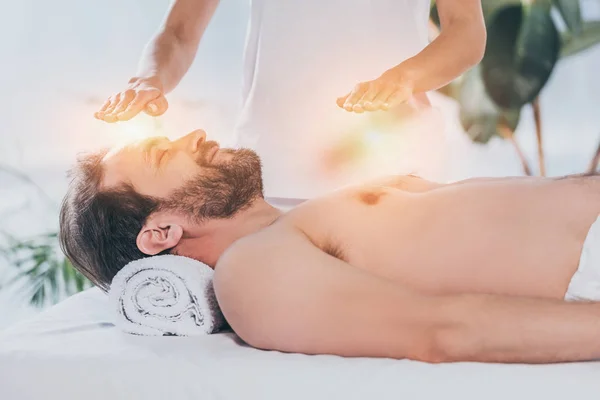 Спокойный бородатый мужчина с закрытыми глазами, лежащий и получающий лечение рейки на голове и груди — стоковое фото