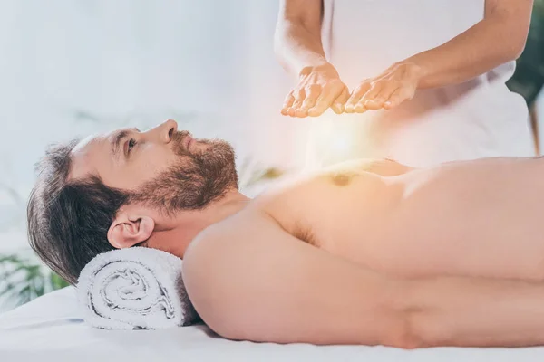 Side view of bearded man looking up while receiving reiki treatment on bare chest — Stock Photo