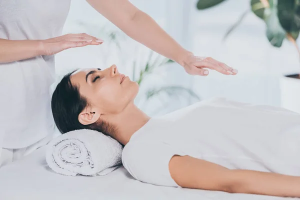 Cropped shot of young woman with closed eyes receiving reiki treatment on head and chest — Stock Photo
