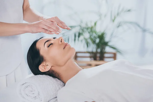 Tiro recortado de calma jovem mulher com olhos fechados recebendo tratamento reiki acima da cabeça — Fotografia de Stock