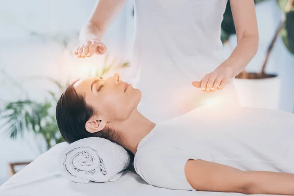 Visão lateral da calma jovem mulher recebendo terapia de cura reiki na cabeça e no peito — Fotografia de Stock