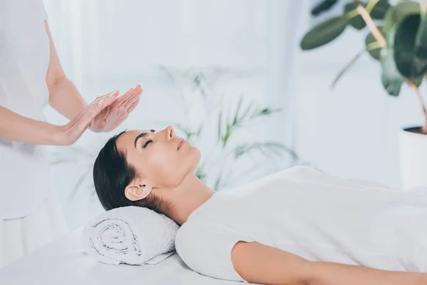 Cropped shot of peaceful young woman with closed eyes receiving reiki treatment on head — Stock Photo