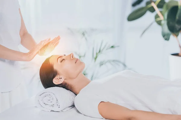 Peaceful young woman with closed eyes receiving reiki treatment on head — Stock Photo