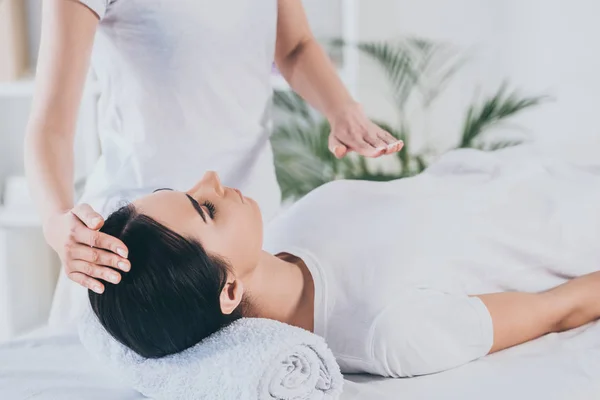 Tiro cortado de pacífica jovem mulher recebendo tratamento de cura reiki na cabeça e no peito — Fotografia de Stock