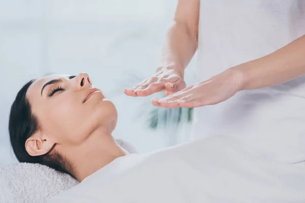 Cropped shot of peaceful young woman with closed eyes receiving healing treatment from reiki practitioner — Stock Photo
