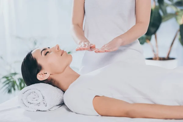 Tiro cortado de pacífica jovem mulher com olhos fechados recebendo tratamento de cura reiki — Fotografia de Stock