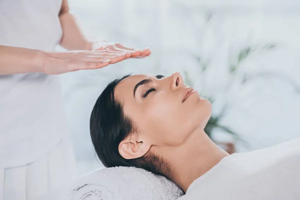 Close-up view of peaceful young woman with closed eyes receiving reiki treatment — Stock Photo