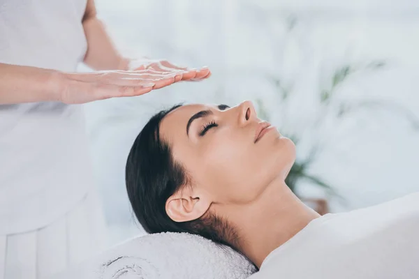 Vista de cerca de una joven pacífica con los ojos cerrados que recibe tratamiento reiki - foto de stock