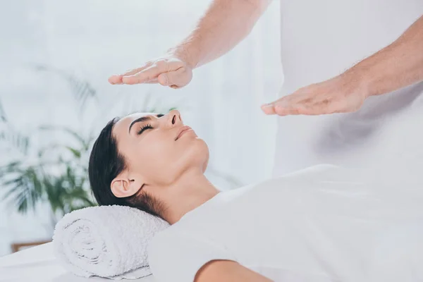 Cropped shot of male healer doing reiki healing session to young woman with closed eyes — Stock Photo